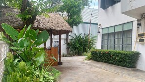 A courtyard with a thatched-roof structure, potted plants, and a white building with large windows. - La nuit de Laos (Luang Prabang)