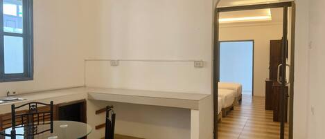 A room with a dining table and chairs, a bench, a window, and a door leading to another room with a bed.