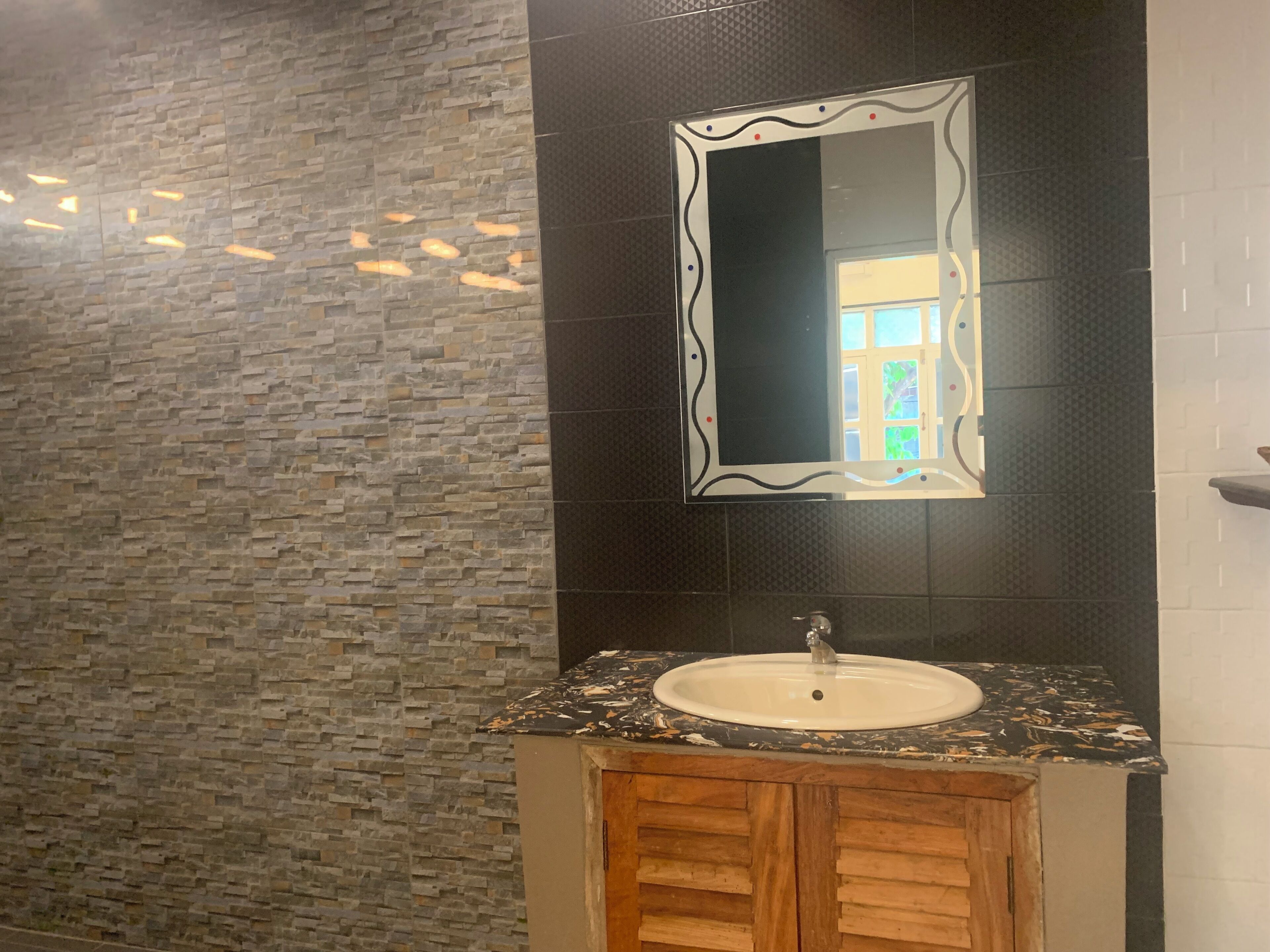Un baño con pared de piedra, un espejo y un lavamanos con mueble de madera.