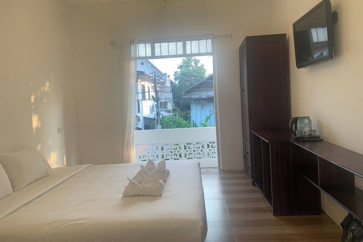 Een hotelkamer met een bed, een aan de muur bevestigde televisie en uitzicht op omliggende gebouwen.