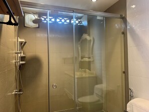 Eine begehbare Dusche mit Glaswänden, einer Handbrause, einer Toilette und einem Handtuchhalter.