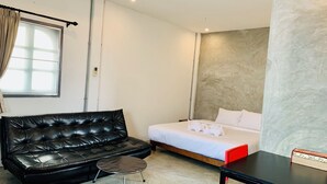 A compact hotel room with a black leather sofa, a small round table, a bed with white linens, and a red chair. - La nuit de Laos (Luang Prabang)