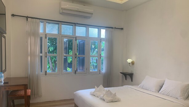 A hotel room with a bed, a chair, a bedside table, a wall-mounted shelf, and a window with curtains. - La nuit de Laos (Luang Prabang)