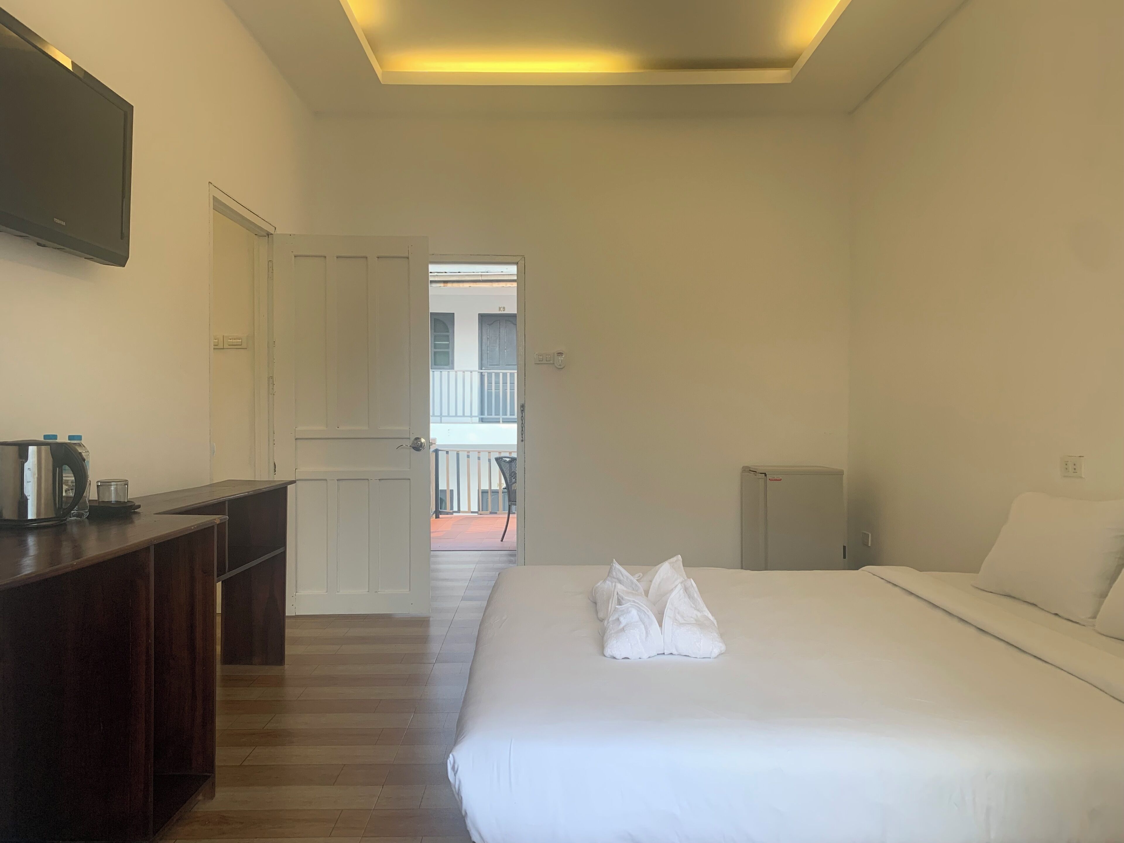 A hotel room with a bed, a desk, a kettle, and a refrigerator.