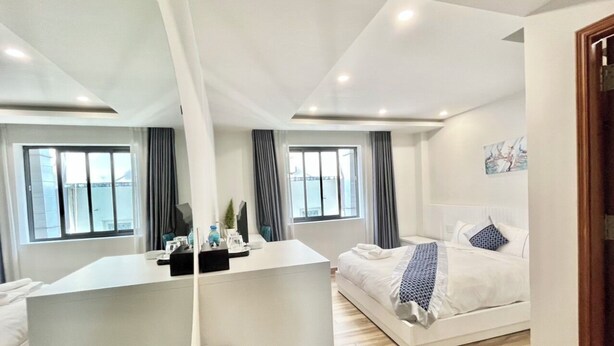 A modern hotel room with a large bed, a desk, and a view of the city through large windows.