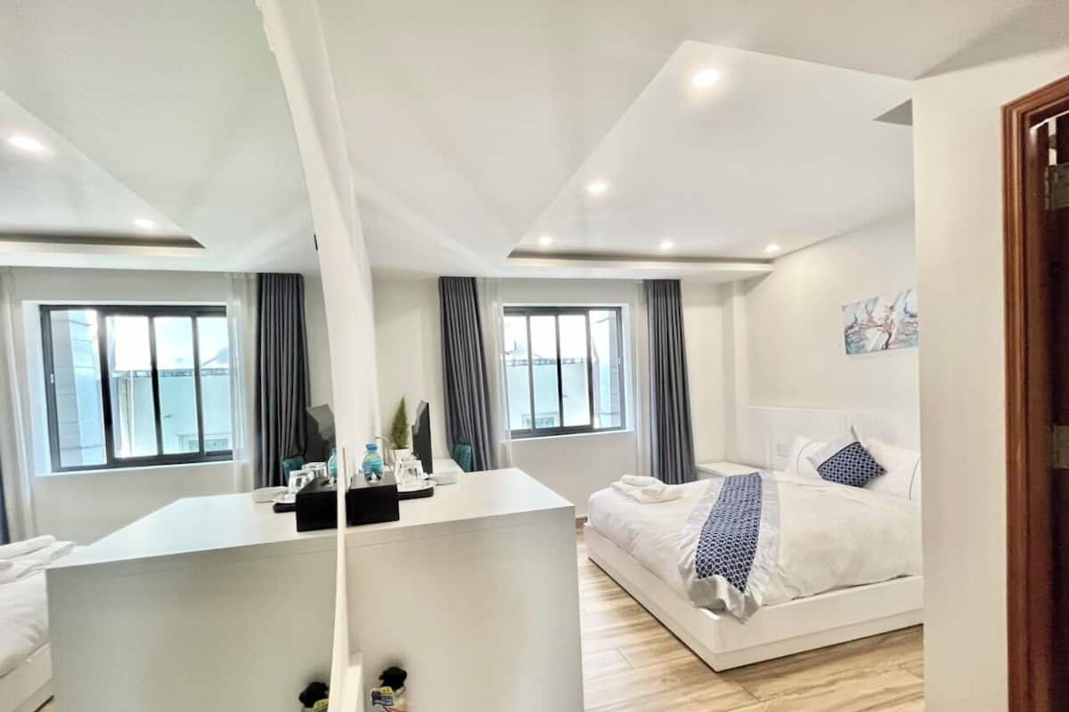Une chambre d’hôtel moderne, dotée d’un grand lit, d’un bureau et offrant une vue sur la ville grâce à de grandes fenêtres.