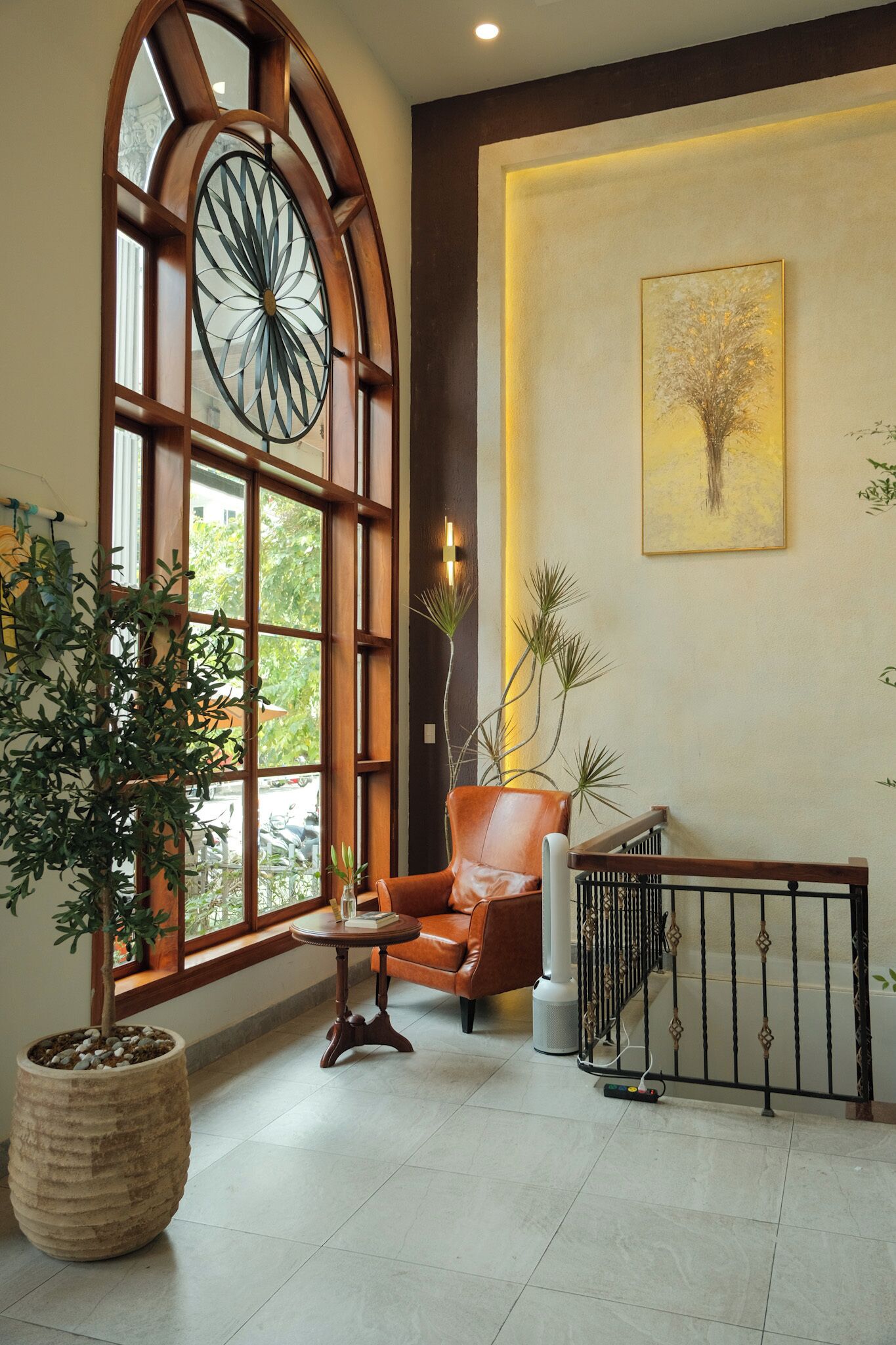Un vestíbulo con un gran ventanal de arco, un sillón de cuero, una planta en maceta, una obra de arte enmarcada y una escalera con barandilla.