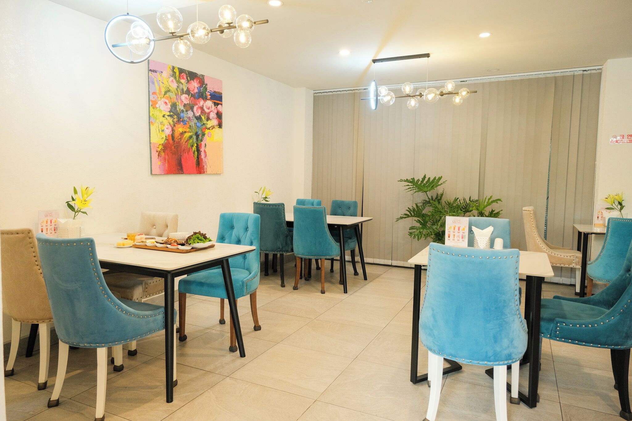 Un coin repas avec des chaises à revêtement bleu, une table blanche et un tableau abstrait aux couleurs vives accroché au mur.