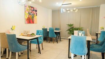 Un coin repas avec des chaises à revêtement bleu, une table blanche et un tableau abstrait aux couleurs vives accroché au mur.