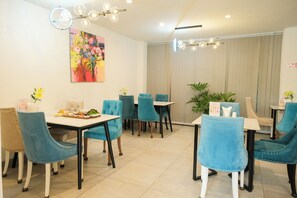 A dining area with blue upholstered chairs, a white table, and a colorful abstract painting on the wall. - Ballantine Hotel Phu My Hung SECC (Ho Chi Minh City)