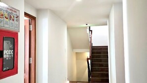 A clean, well-lit hallway with a fire hose call sign, a staircase, and a wooden door.