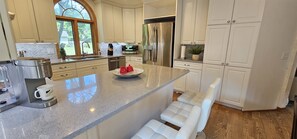 A modern kitchen with white cabinetry, a stainless steel refrigerator, and a granite countertop.