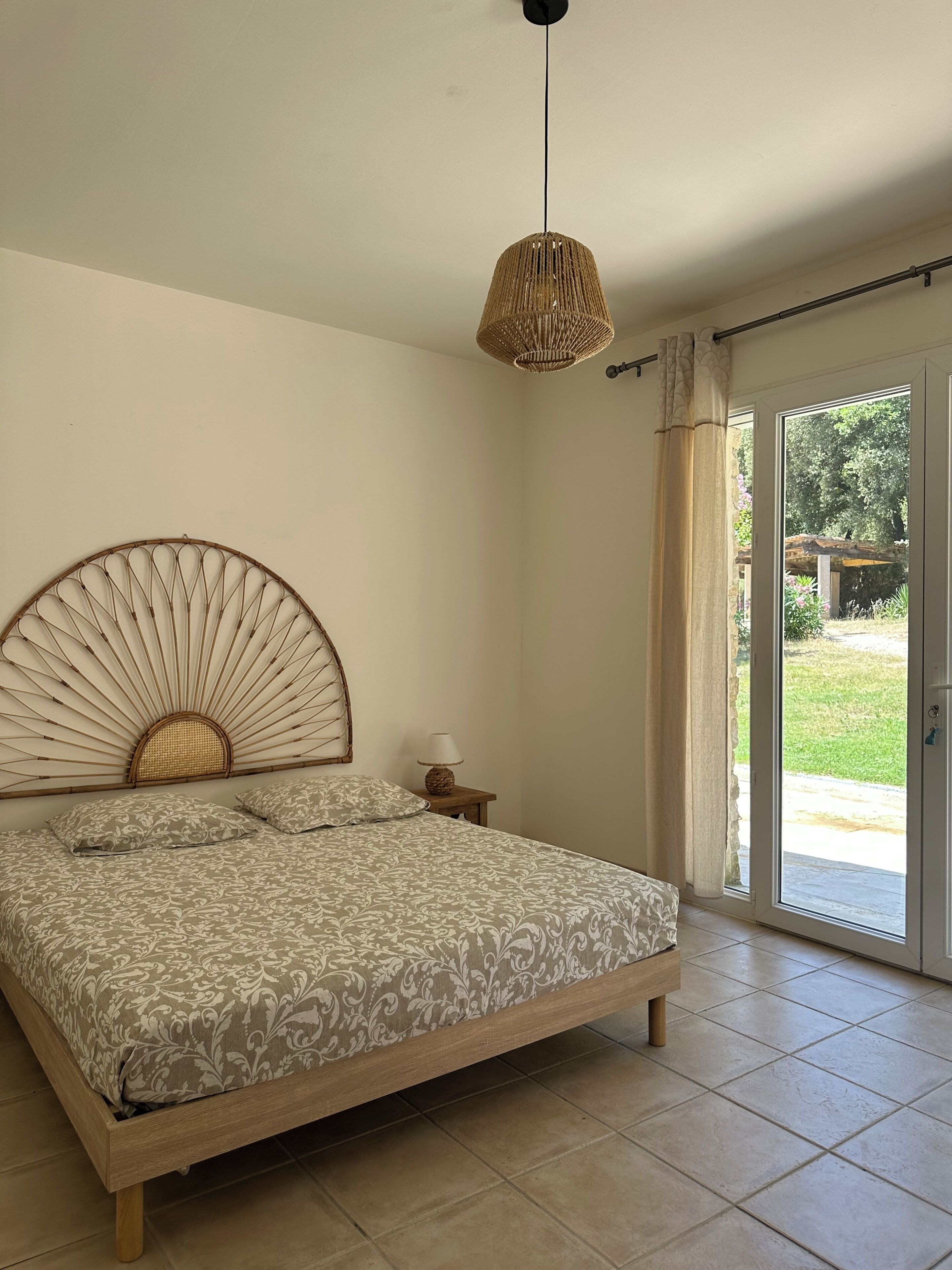Une chambre à coucher comprenant un lit, une lampe de chevet, un luminaire suspendu et une porte-fenêtre coulissante donnant sur un espace extérieur.