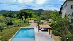 Zona de piscina con una pérgola, rodeada de abundante vegetación y un muro de piedra.