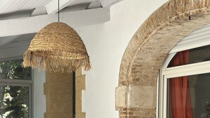 Una habitación con pared de ladrillo, lámpara de techo tejida, silla de mimbre y puerta de cristal con cortina.