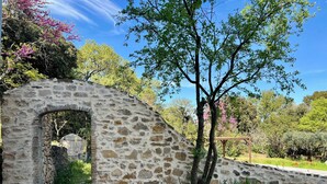Un arco de piedra que da acceso a un jardín con muro de piedra, rodeado de árboles y vegetación.