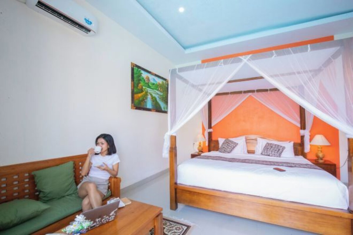 A bedroom with a bed under a canopy, a wooden headboard, a nightstand with a lamp, and a green sofa.