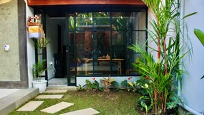 A modern building entrance with a glass door, a small garden area with stepping stones, and various potted plants. - Ubud Arindra Private Pool Villa (Ubud)