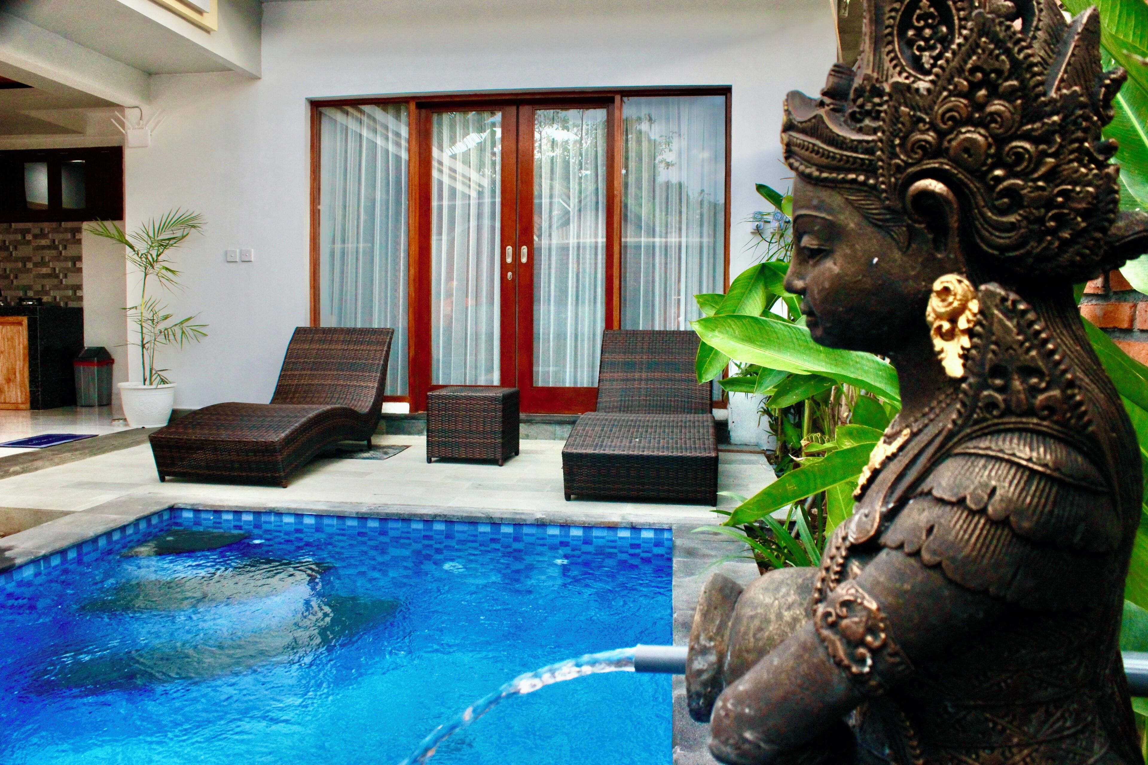 A statue by a swimming pool with a sliding glass door in the background.