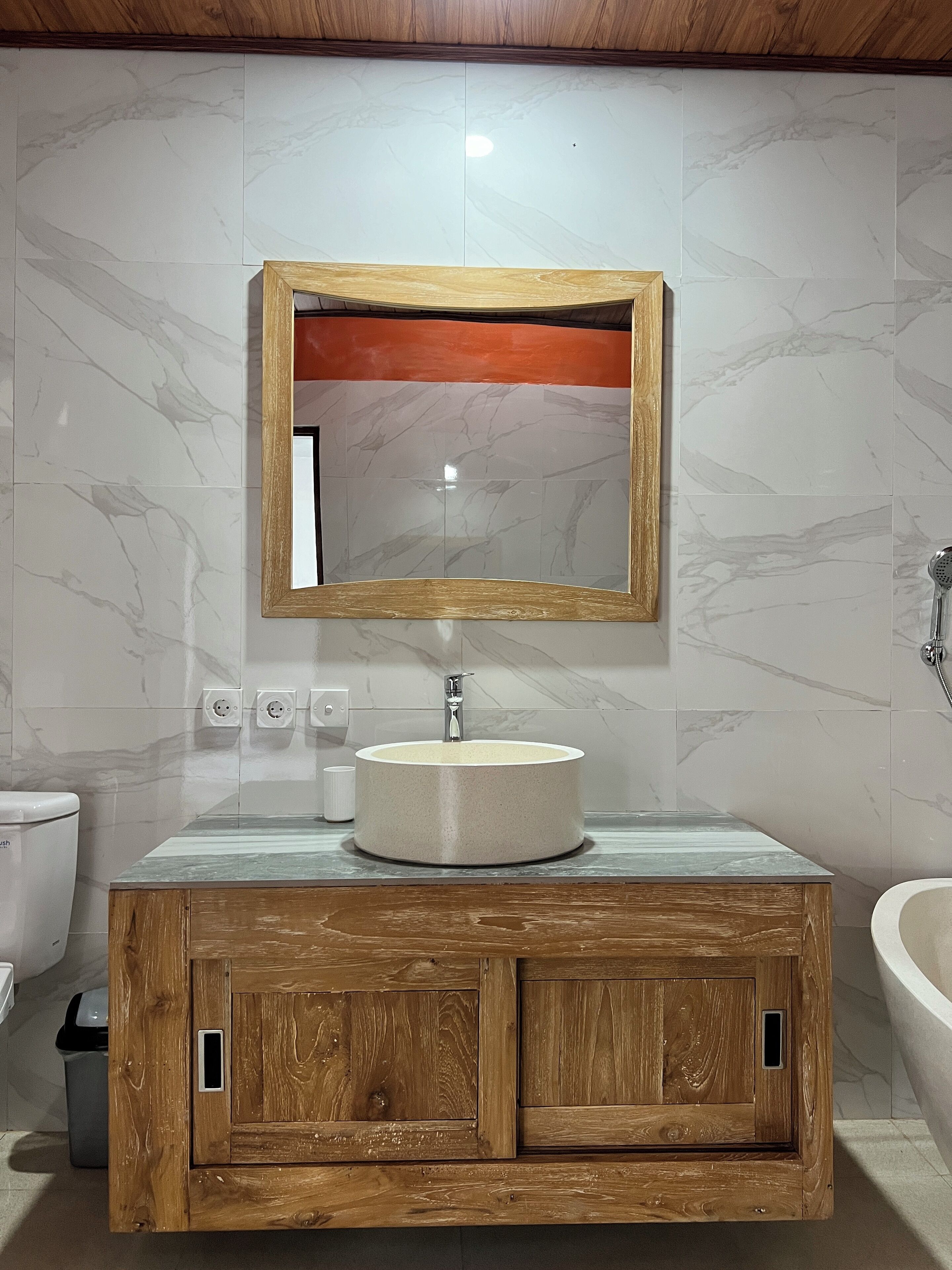 A bathroom with a wooden vanity, a round sink, and a mirror with a wooden frame.