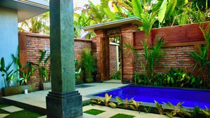 A pool area with a brick wall, potted plants, and a tiled floor. - Ubud Arindra Private Pool Villa (Ubud)