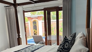 A bedroom with a large bed, a view of the outside, and a balcony with a chair. - Ubud Arindra Private Pool Villa (Ubud)