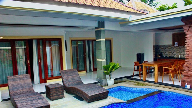 A swimming pool with lounge chairs, a dining table, and a kitchen area. - Ubud Arindra Private Pool Villa (Ubud)
