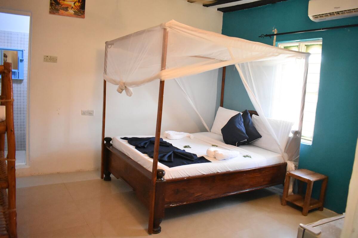 Una cama con dosel, un taburete de madera y una ventana con vistas.