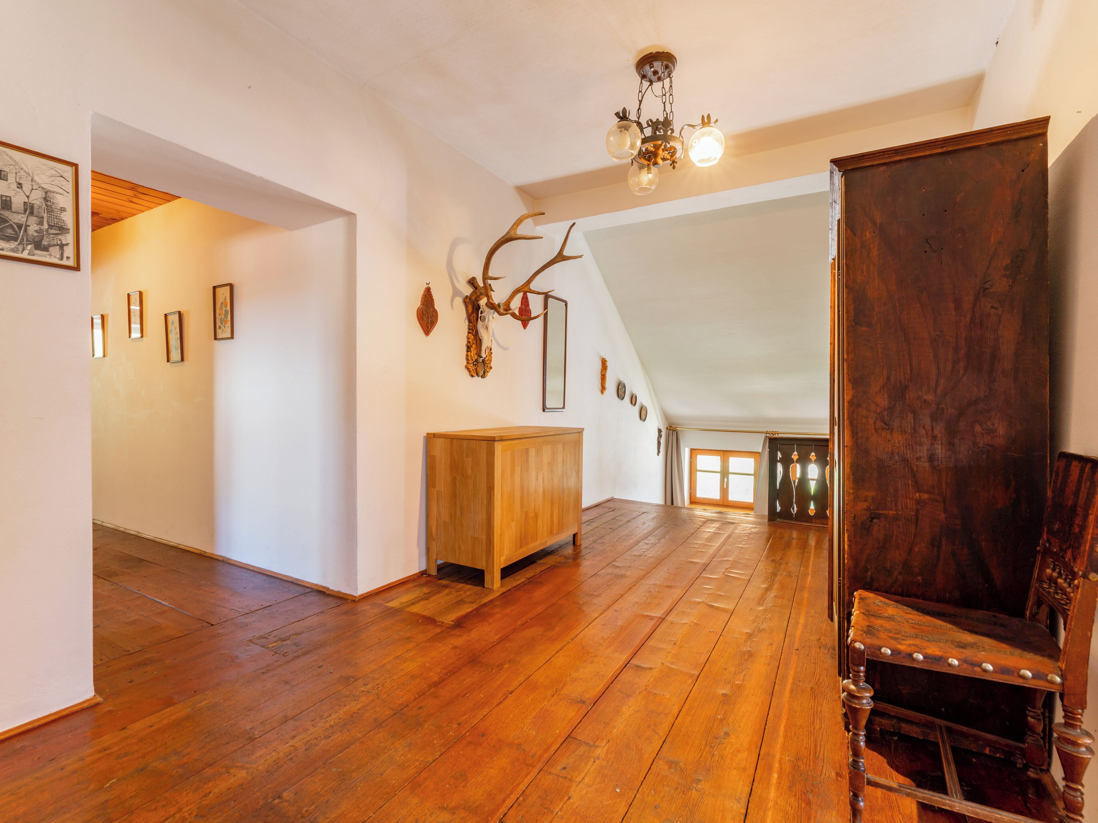 A spacious room with wooden flooring, a wooden cabinet, and a large dark wooden chair.