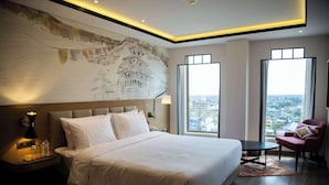 Habitació d'hotel moderna amb un llit gran, una tauleta de nit, un escriptori, una cadira i grans finestres que donen vista a la ciutat.