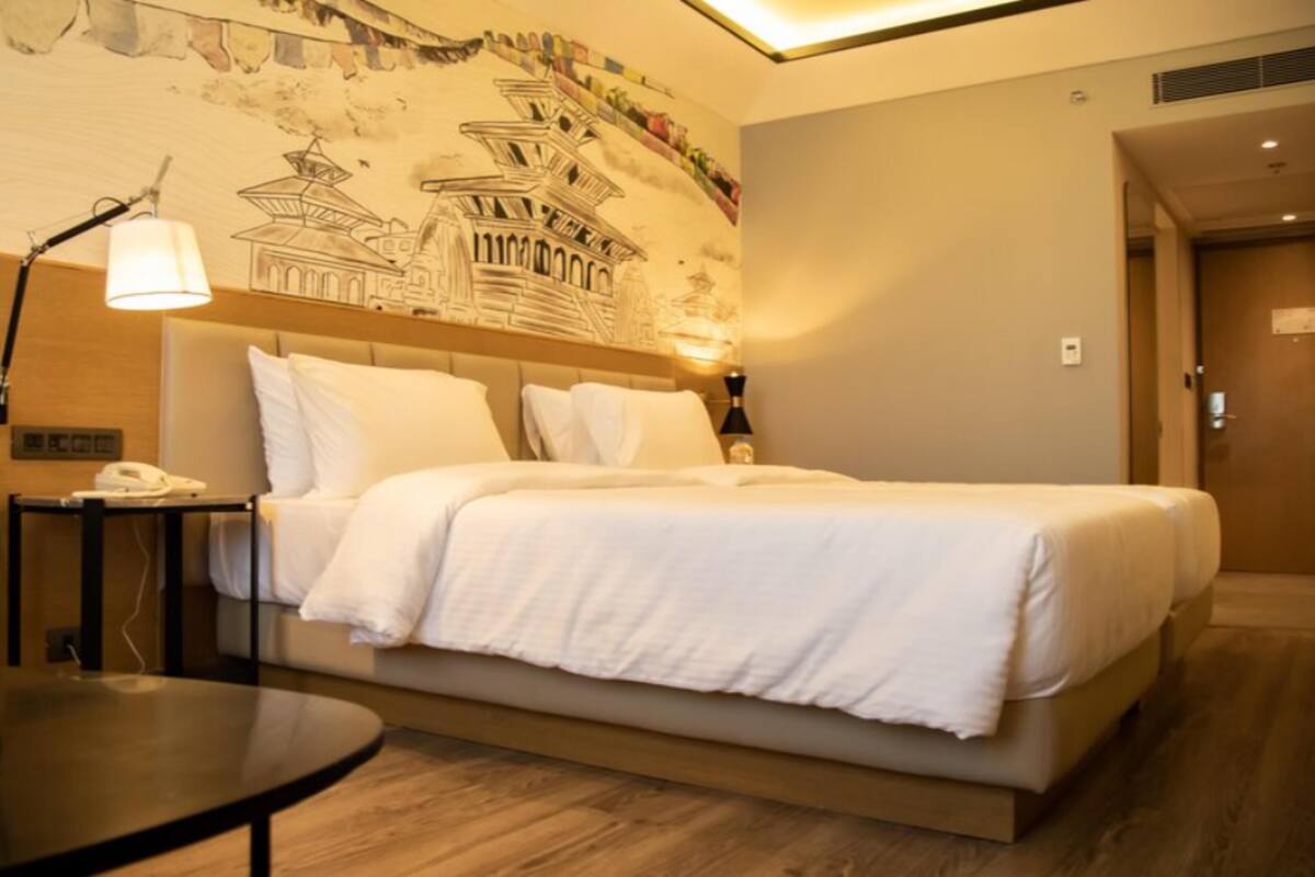 A hotel room with a bed, bedside tables, a lamp, and a wall mural.