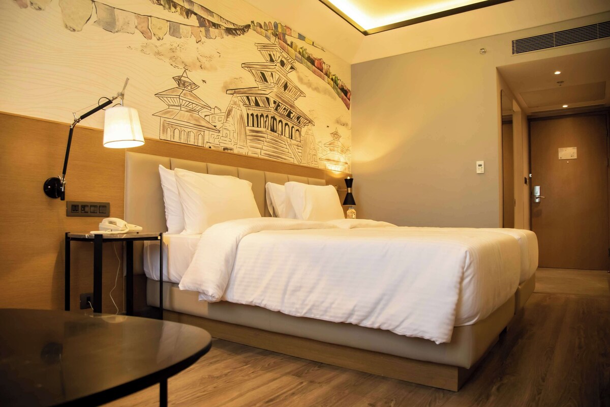 A hotel room with a bed, bedside lamp, bedside table, and a wall mural.