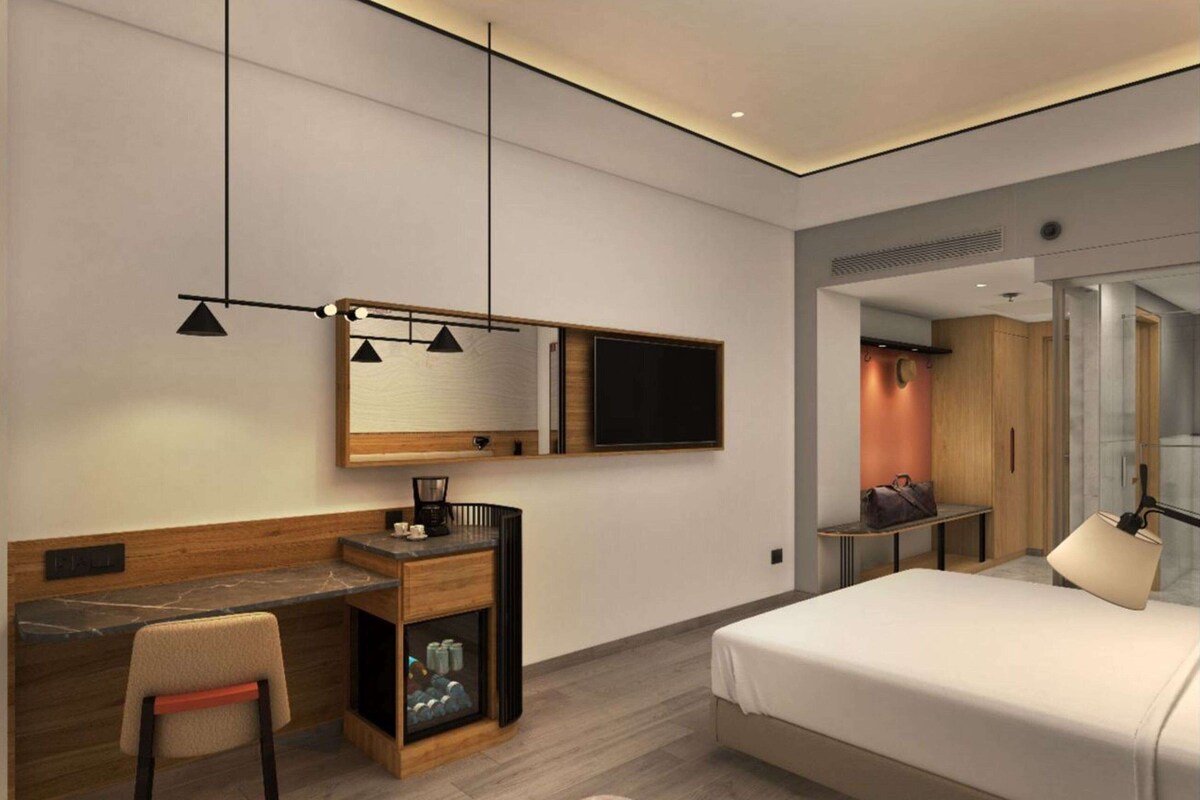 A modern hotel room with a bed, desk, chair, and a television.