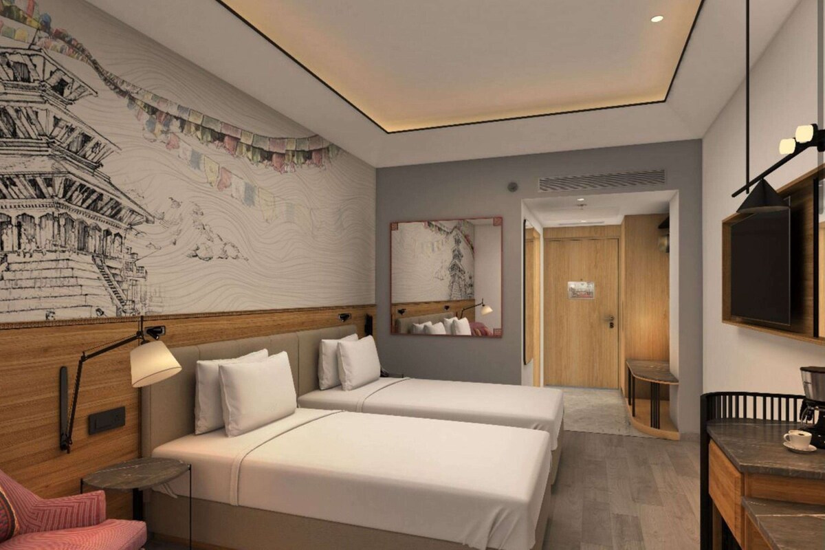 A hotel room with two beds, a desk, a chair, a lamp, a mirror, and a wall with a mural.