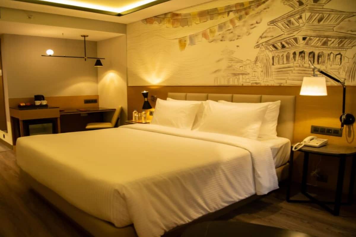 A hotel room with a large bed, a desk, a chair, a lamp, and a wall with a map.