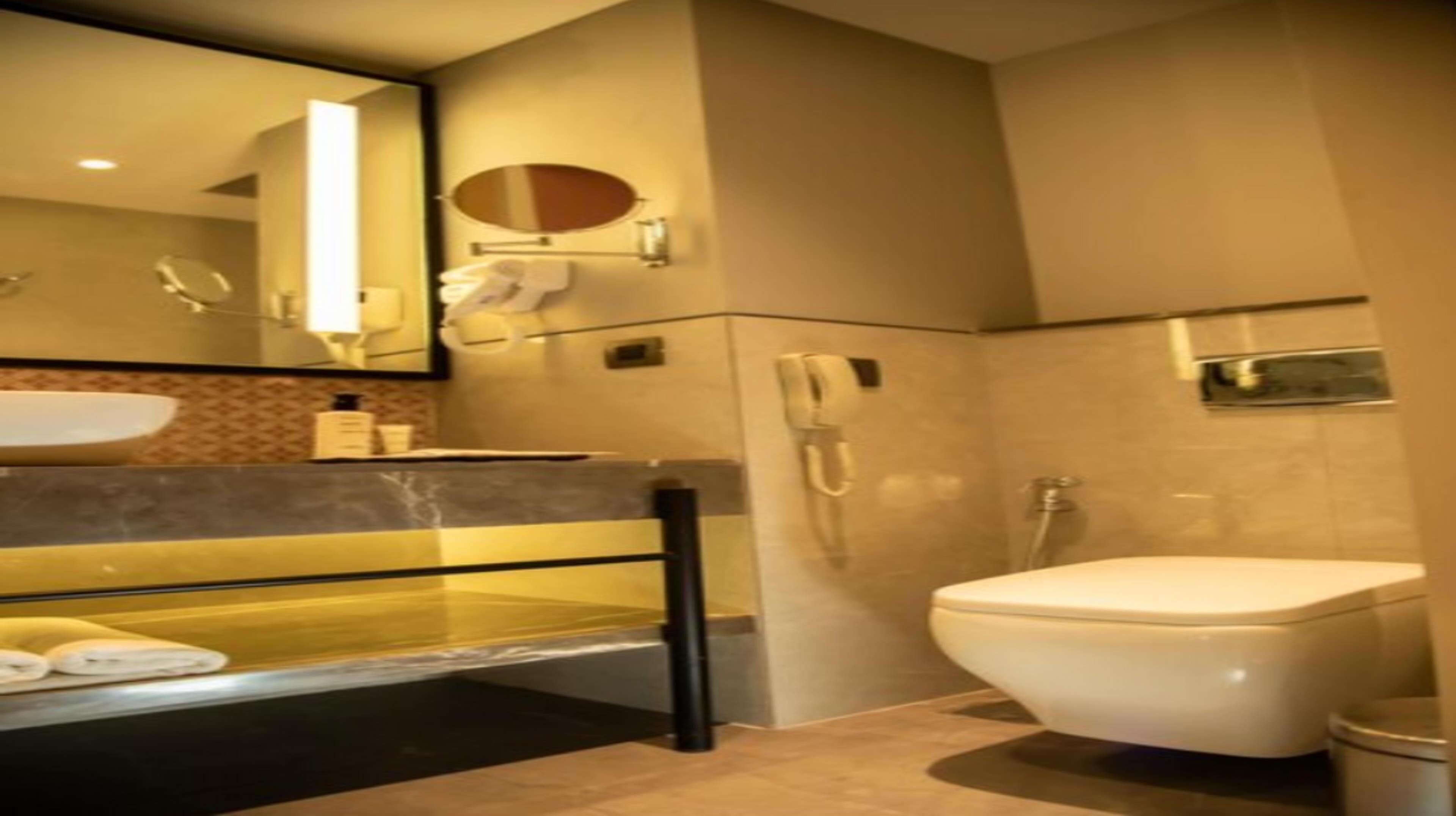 A modern bathroom with a marble sink, a toilet, a mirror, and a shower.