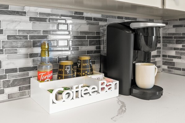 Una estación de café con cafetera, jarabe Torani y tazas de café.