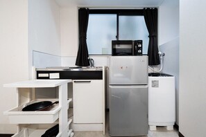 A compact kitchen with a refrigerator, microwave, and a small water dispenser. - GLOU Shinjuku Family (Tokyo)