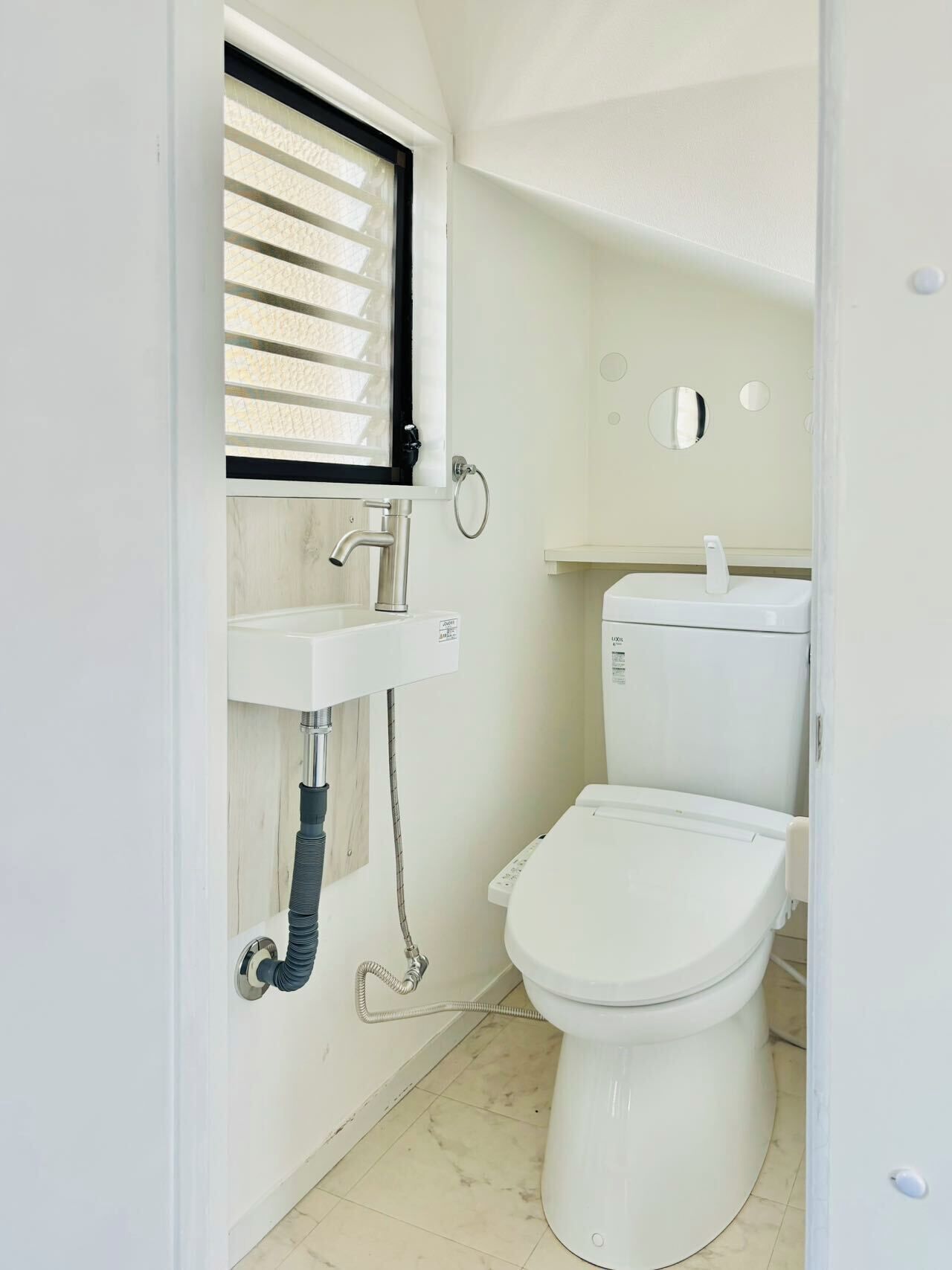 Une petite salle de bain compacte, équipée de toilettes, d’un lavabo et d’une fenêtre avec stores.
