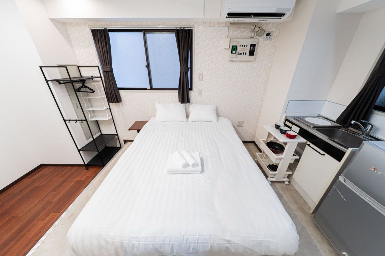 A hotel room with a bed, a desk with a sink, a wardrobe, and a window with curtains.
