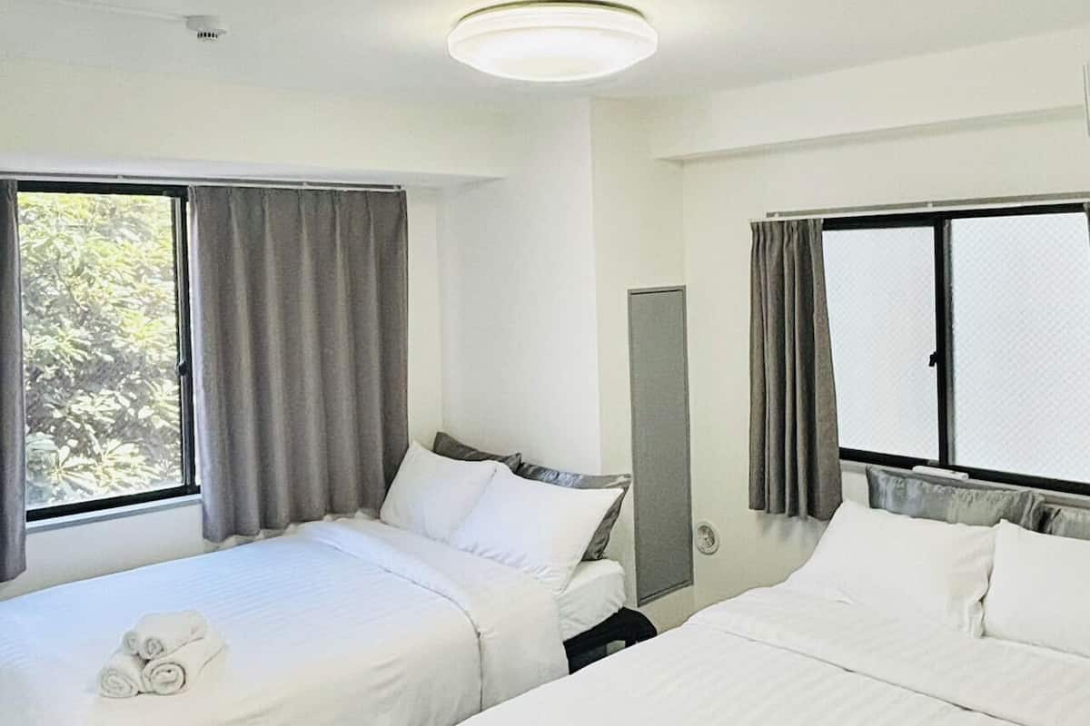 A hotel room with two single beds, a large window with curtains, a ceiling light, and a wall-mounted mirror.