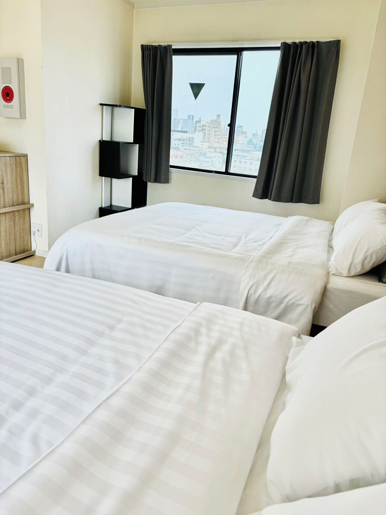 Une chambre d’hôtel avec deux lits, une vue sur la ville, une lampe noire et un meuble en bois.