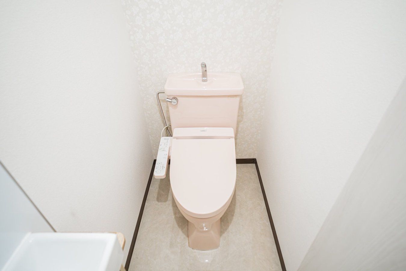 A small, compact bathroom with a toilet, a bidet attachment, and a wall-mounted faucet.