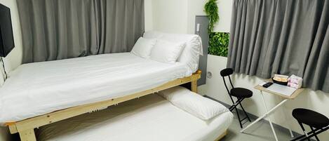 A small, single-room accommodation with a bunk bed, a desk, two chairs, and a small window with curtains.
