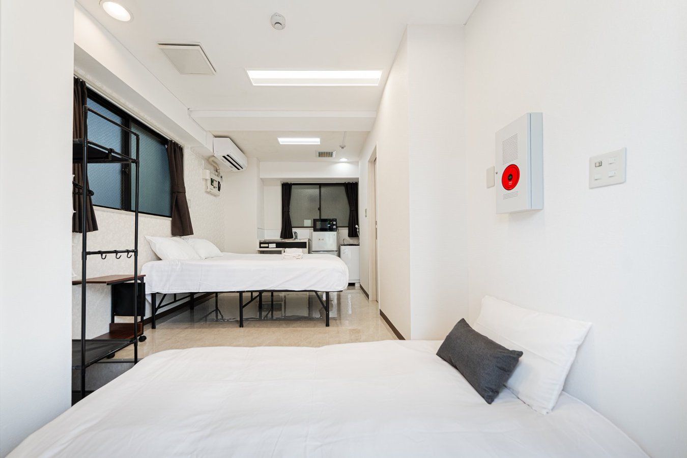 A hotel room with two beds, a desk, a chair, a microwave, and a red emergency alarm.