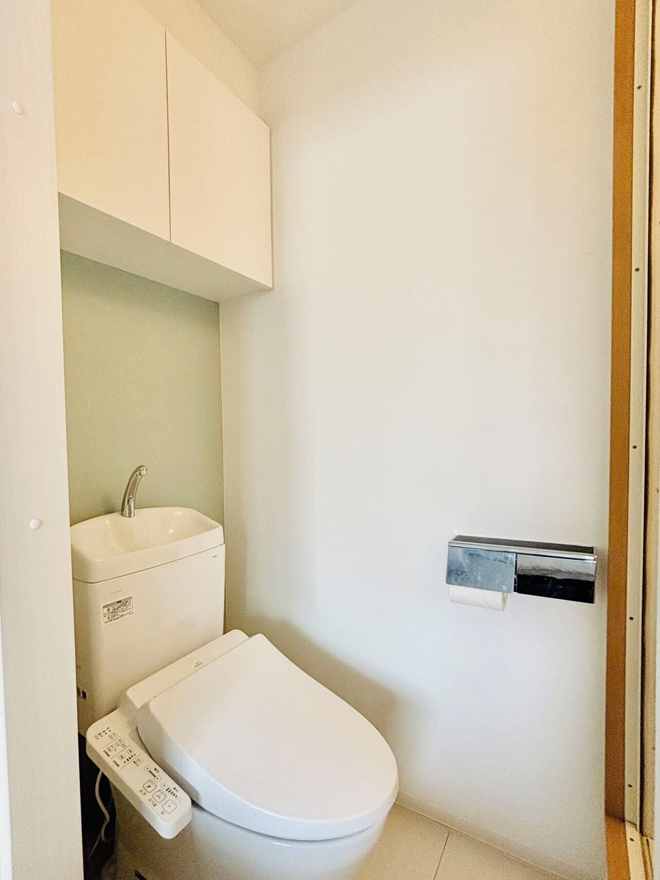 A small, clean bathroom with a white toilet, a sink, and a paper towel dispenser.