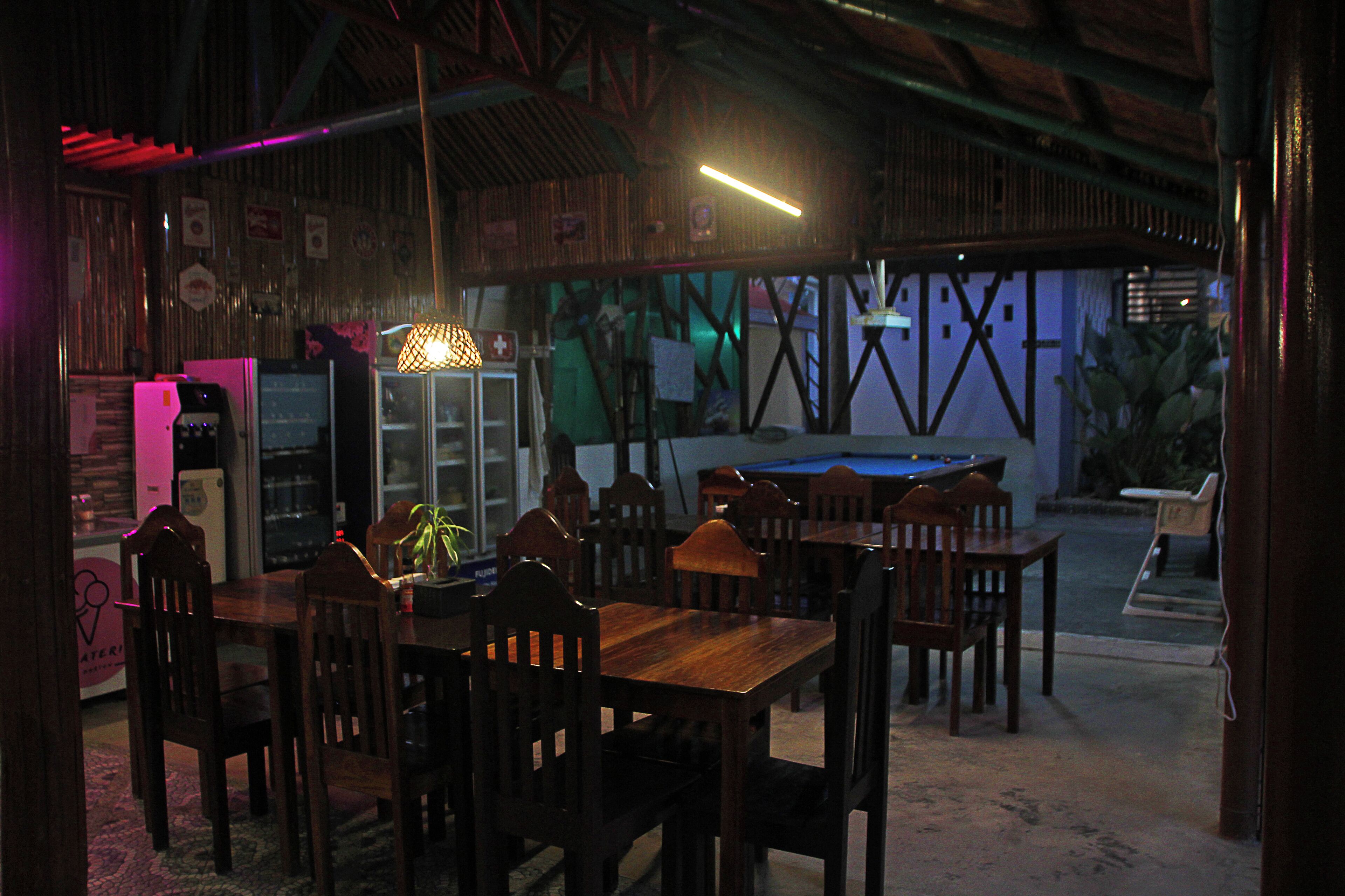 Un comedor interior con poca luz, mesas y sillas de madera, una mesa de billar y una luz de neón.