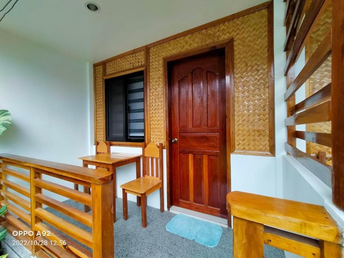 A wooden balcony with a table and chairs, a wooden door, and a window with a black blind.