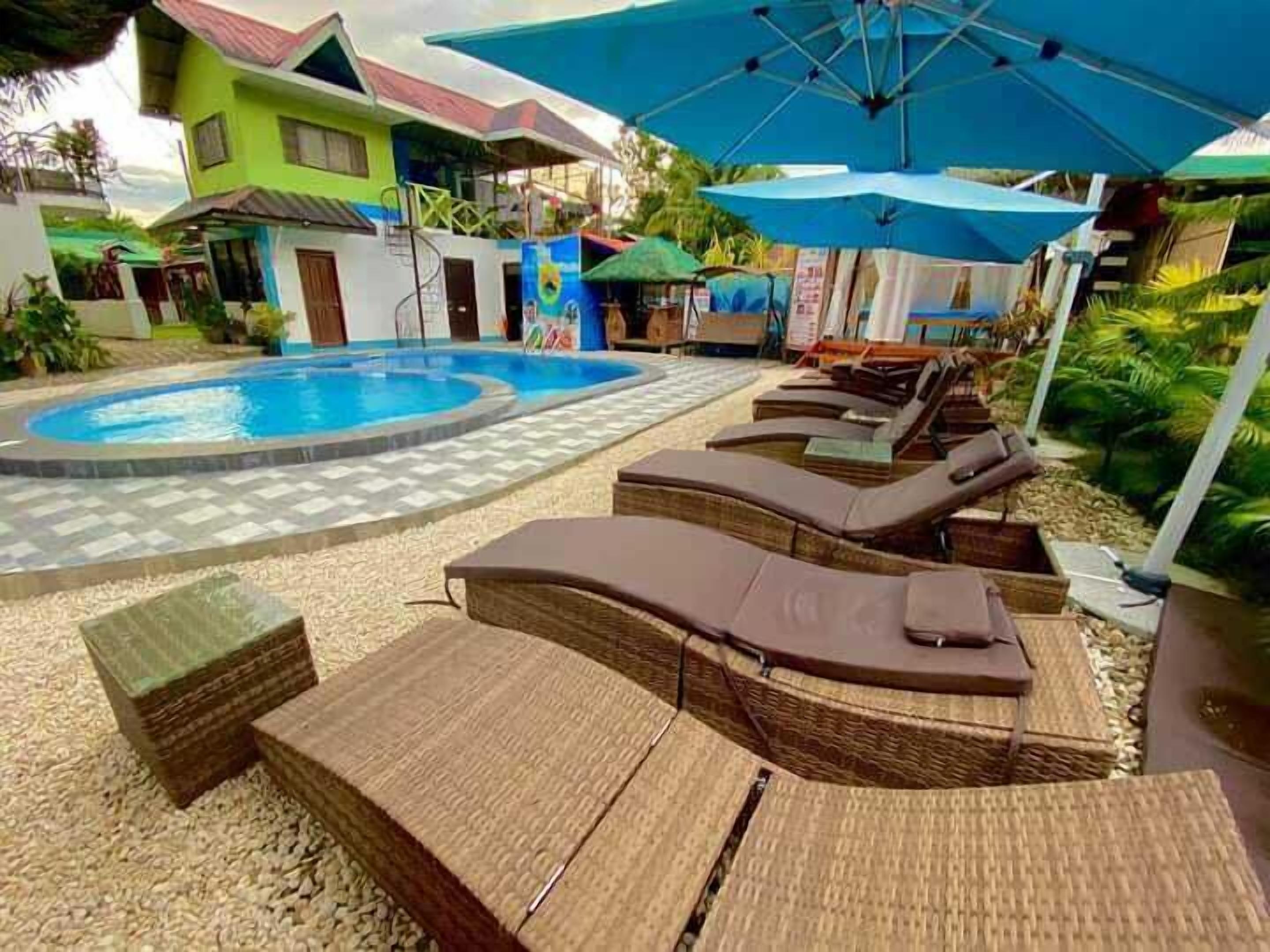 Un espace piscine doté de chaises longues et de parasols, entouré de bâtiments aux façades colorées.