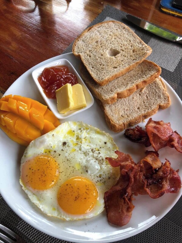 Une assiette avec des œufs, du bacon, des toasts, du beurre et de la mangue.